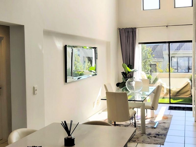 Bright open-plan living and dining area featuring double-volume ceilings, tiled floors, and large sliding doors leading to an outdoor patio space.