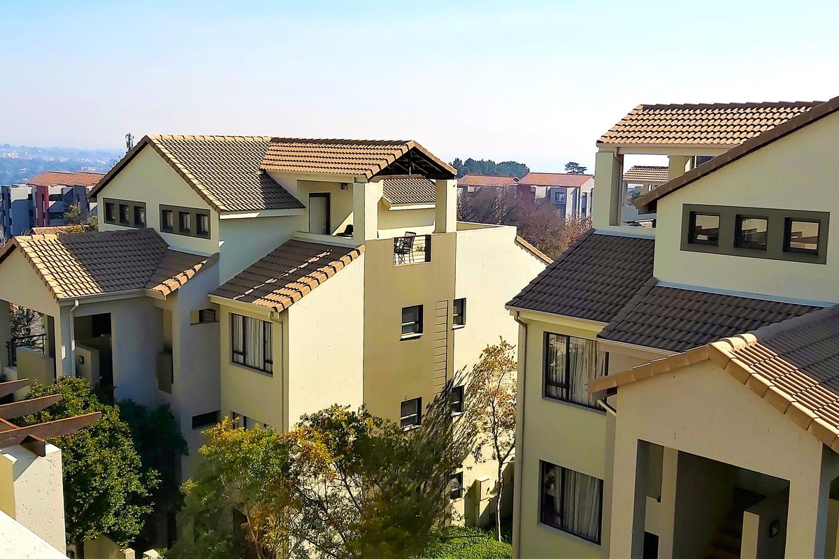 An elevated view of the apartment complex exterior, showcasing the multi-level architecture, tiled roofing, and private balconies.
