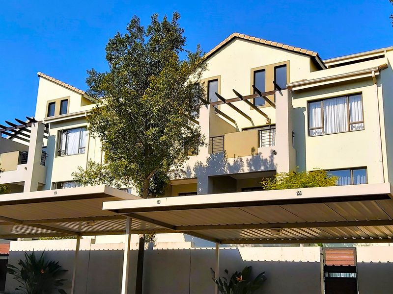 A well-maintained apartment complex exterior featuring covered parking bays, private balconies with pergolas, and modern architectural design.