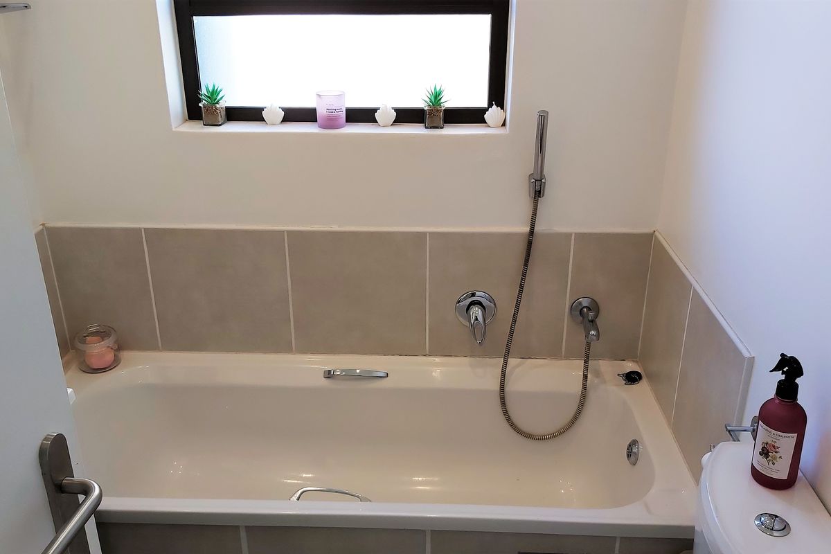A clean bathroom featuring a built-in bathtub with a handheld shower attachment, tiled splashback, and a toilet.