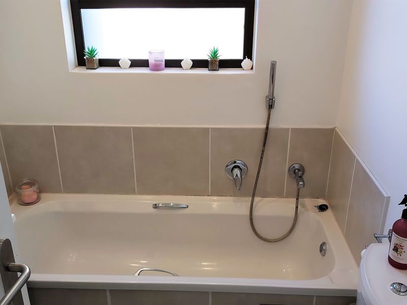 A clean bathroom featuring a built-in bathtub with a handheld shower attachment, tiled splashback, and a toilet.