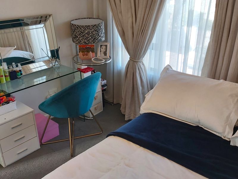 A well-maintained bedroom featuring neutral wall tones, carpeted flooring, and large windows dressed with elegant floor-to-ceiling curtains.