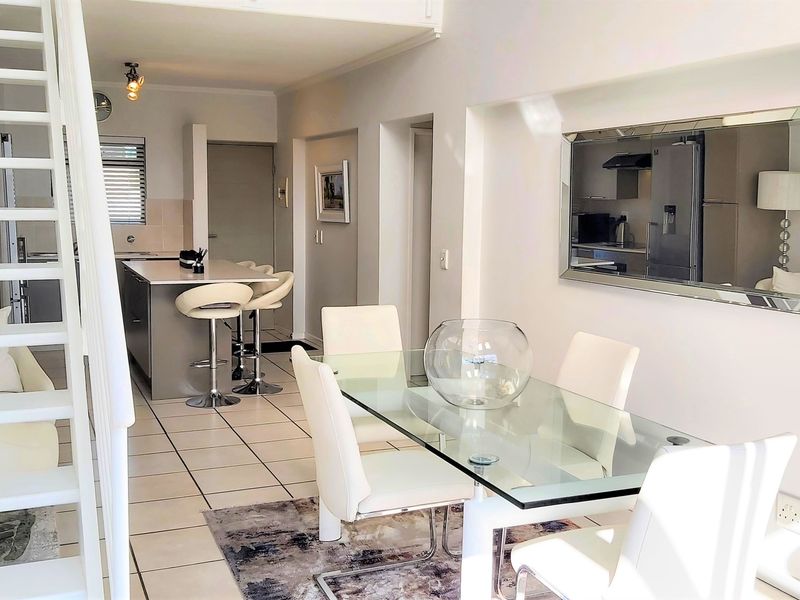 Bright open-plan living and dining area featuring a modern kitchen island, tiled flooring, and a staircase leading to an upper level.