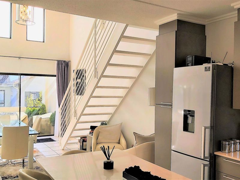 Open-plan living area featuring a modern kitchen, tiled flooring, and a staircase leading to the upper level with access to a patio.