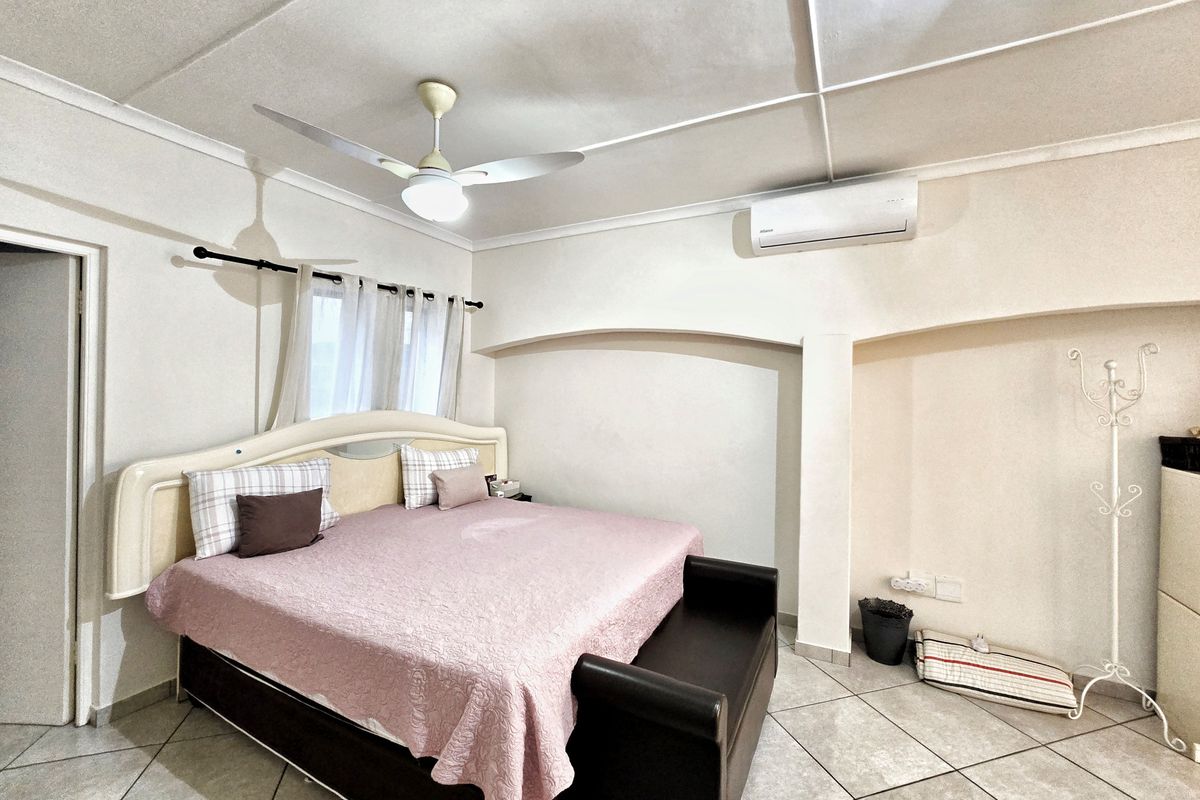 A spacious bedroom featuring tiled flooring, a ceiling fan, and a wall-mounted split-system air conditioner.