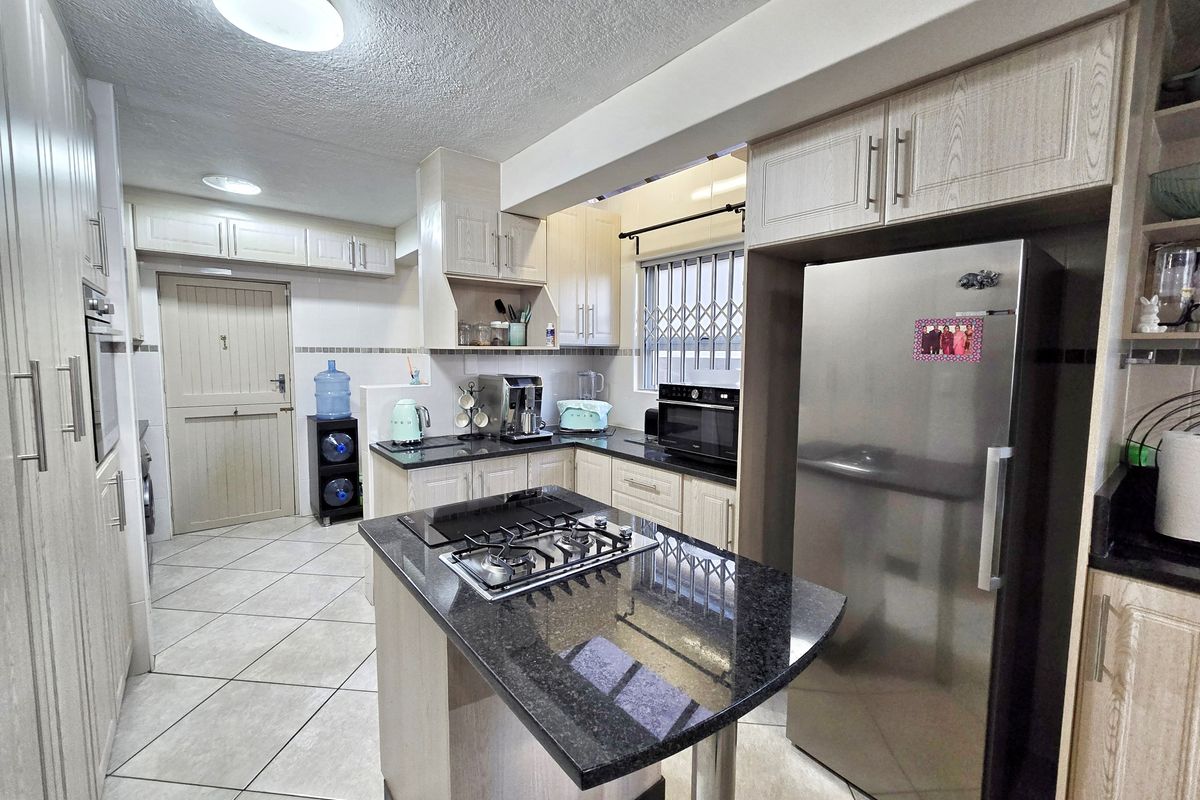 Functional kitchen featuring granite countertops, built-in oven, gas hob, and ample laminated cabinetry with tiled flooring and a secure window.