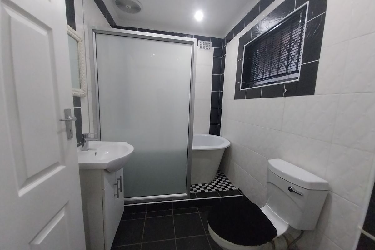 A modern bathroom featuring a freestanding bathtub, separate shower enclosure, vanity basin, and toilet with contrasting black and white tiled finishes.