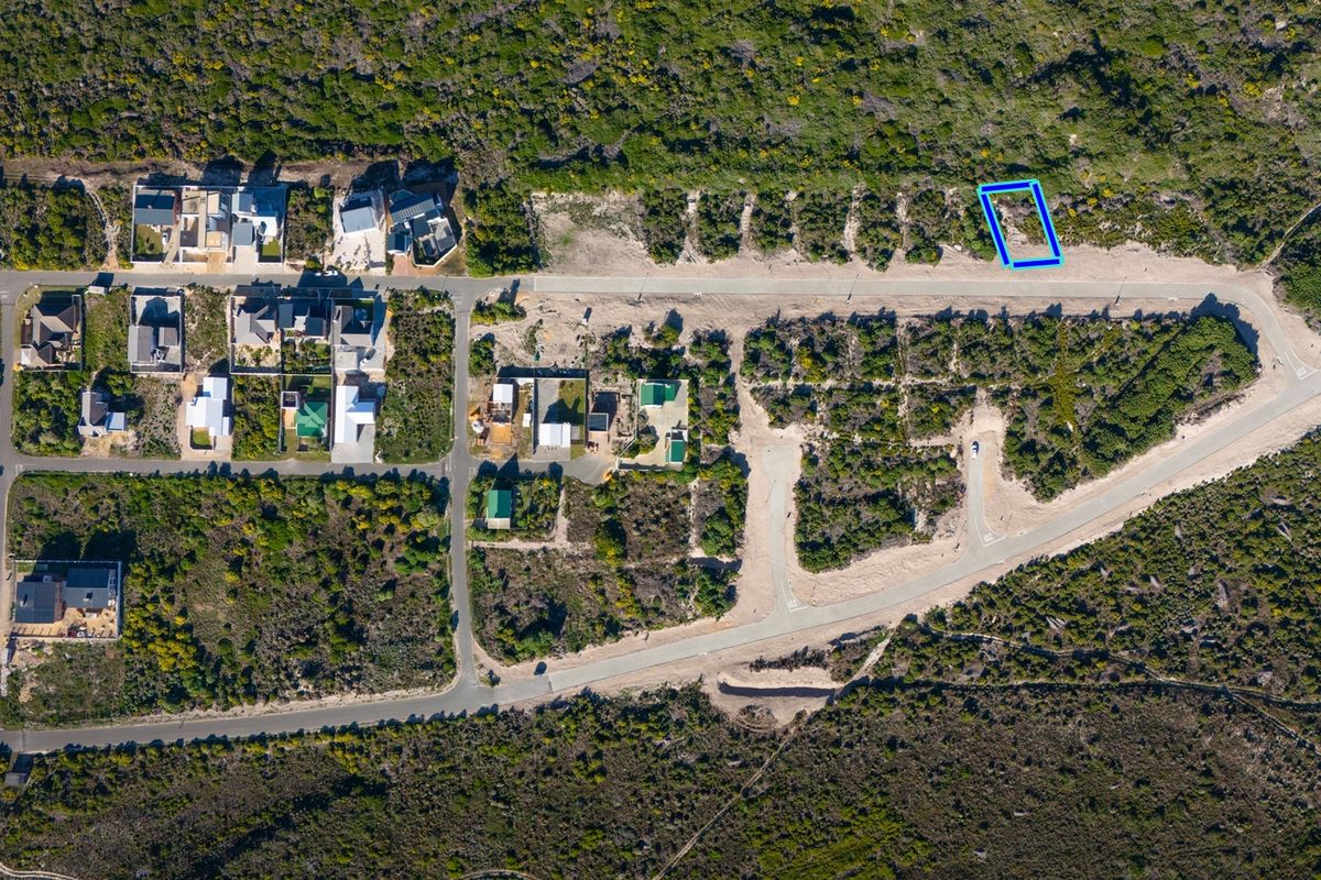 An aerial view of a residential vacant land plot situated within a developed coastal estate, featuring direct road access and surrounding natural vegetation.