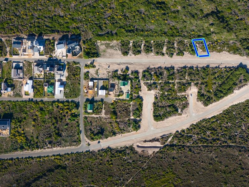 An aerial view of a residential vacant land plot situated within a developed coastal estate, featuring direct road access and surrounding natural vegetation.
