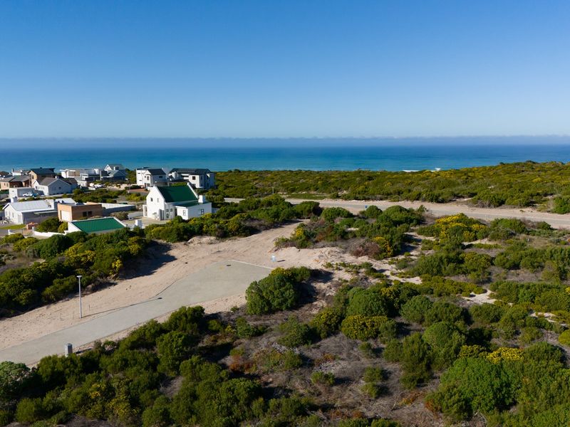 Aerial view of a vacant residential plot featuring a paved driveway, surrounded by coastal vegetation with ocean views in the background.