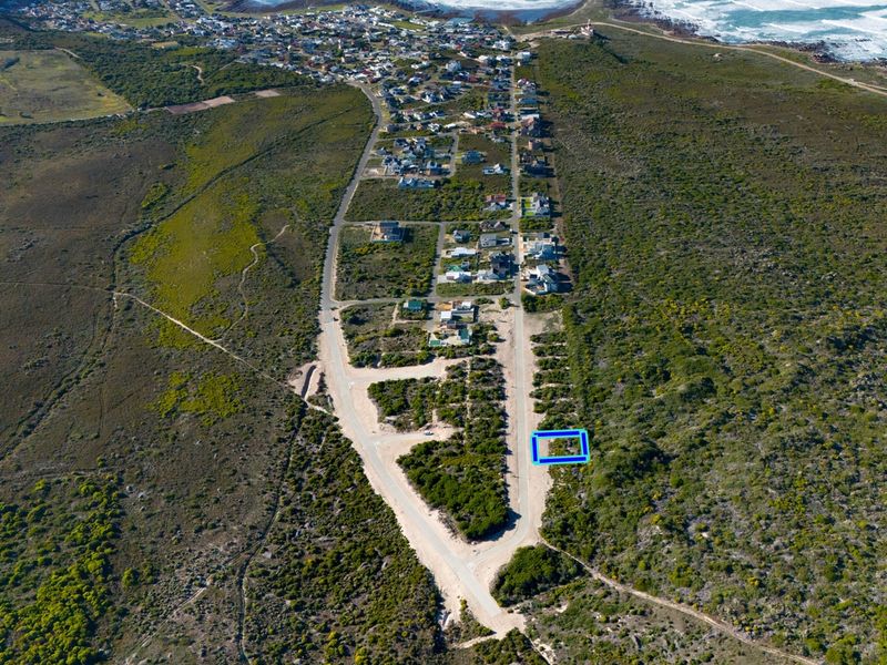 Aerial view of a vacant residential plot situated in a coastal development with established road access and proximity to the ocean.