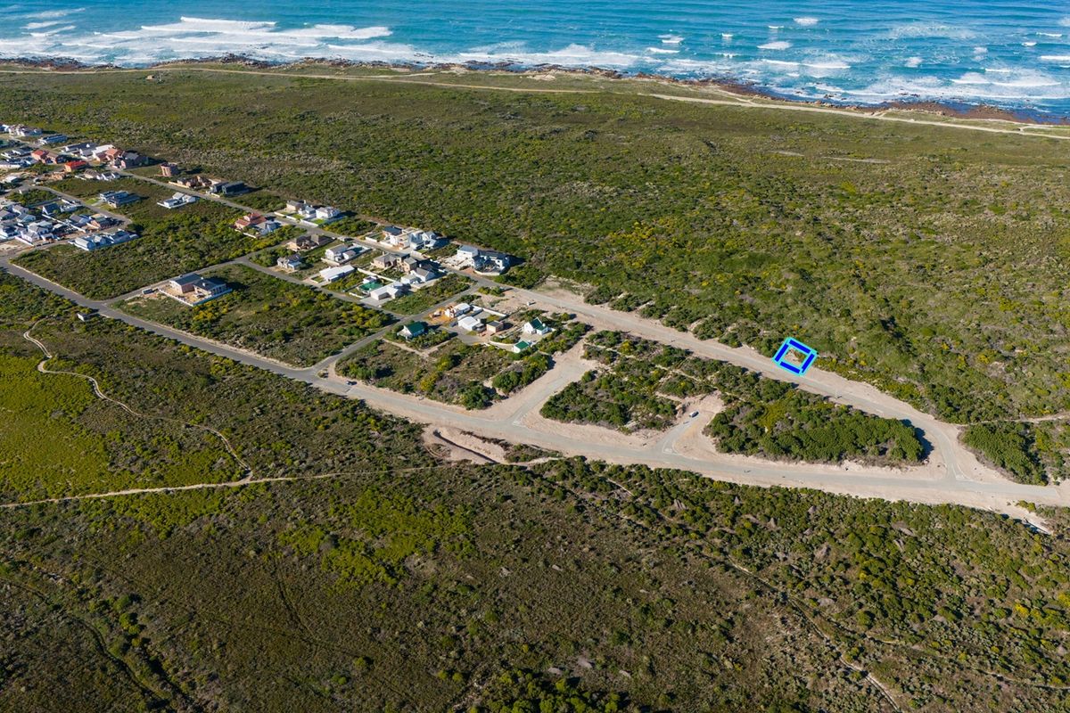 Aerial view of a vacant residential plot situated in a coastal development with nearby road access and ocean proximity.