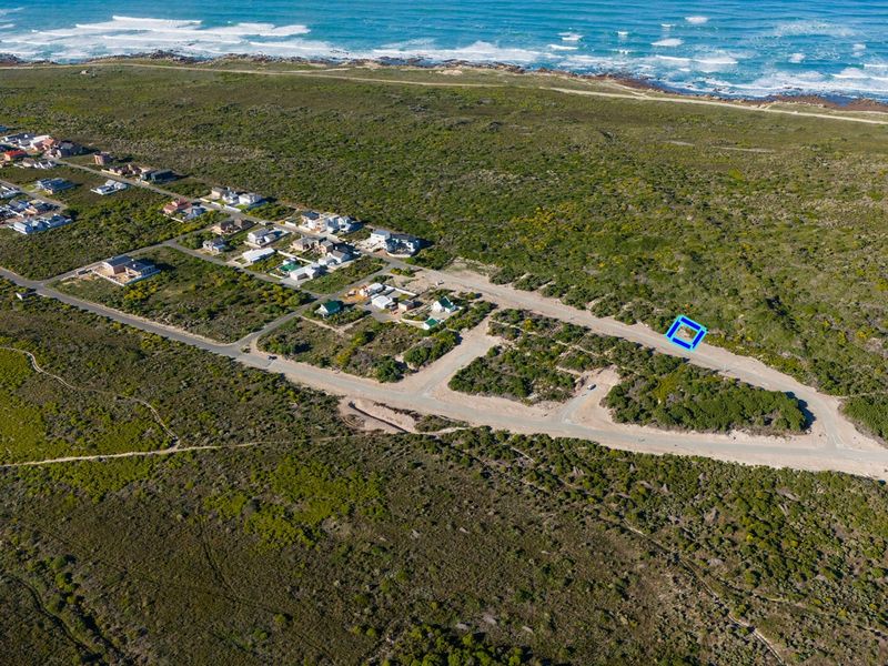 Aerial view of a vacant residential plot situated in a coastal development with nearby road access and ocean proximity.