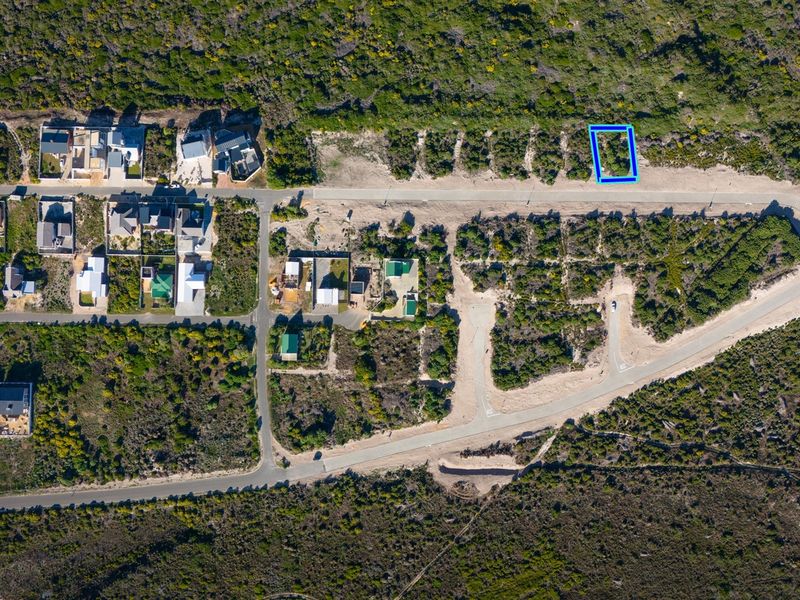 Aerial view of a vacant residential plot highlighted in blue, situated within a developed coastal neighborhood with established road infrastructure.