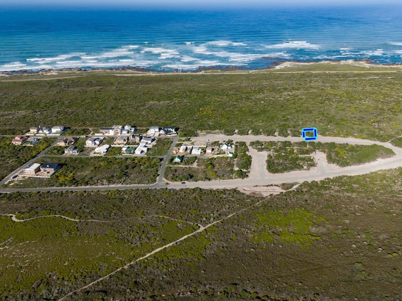 Aerial view of a vacant residential plot situated in a coastal development with established road infrastructure and proximity to the ocean.