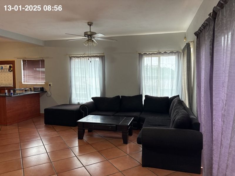 Open-plan living area featuring tiled flooring, a ceiling fan, and a breakfast bar connecting to the kitchen space.