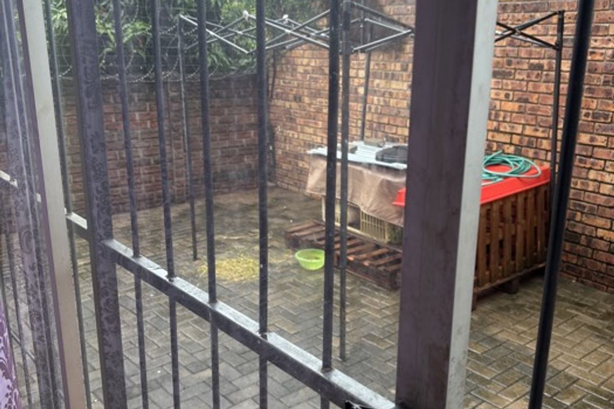 A small, enclosed rear courtyard featuring brick boundary walls, paved flooring, and a security gate.