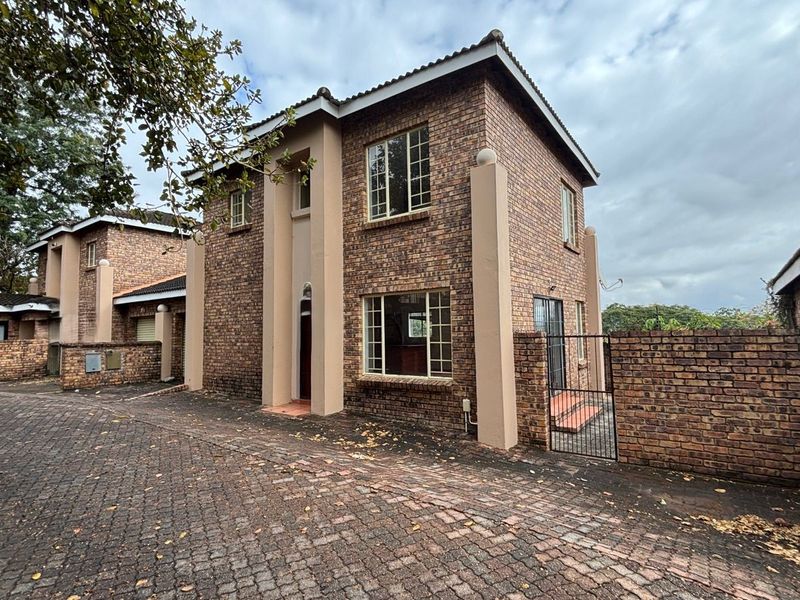 A two-story face-brick residential property featuring a paved driveway, perimeter walling, and secure gated access in a suburban setting.