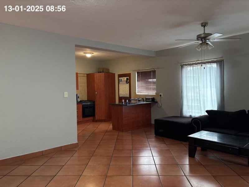 Open plan living area featuring tiled flooring, a ceiling fan, and a functional kitchen with built-in cabinetry and oven.