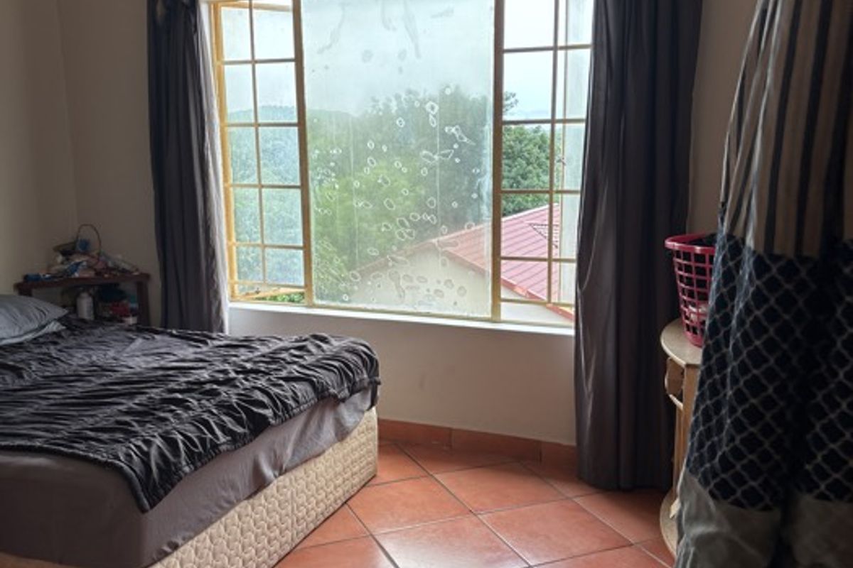 A bedroom featuring tiled flooring, a ceiling fan, and a large window with security bars overlooking the exterior.