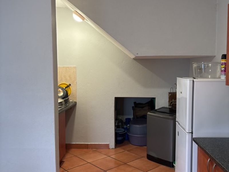 A functional scullery or utility area featuring tiled flooring, built-in cabinetry, and a convenient under-stair storage alcove.
