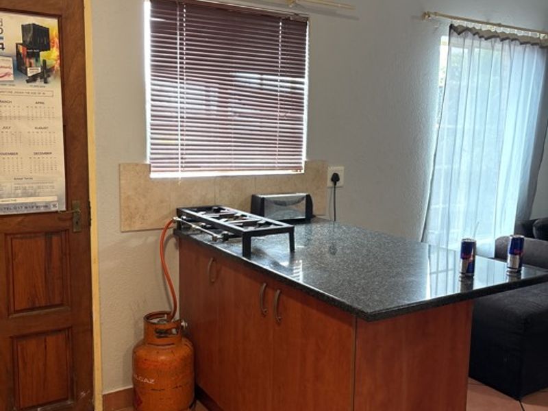 A compact kitchen area featuring wooden cabinetry, a granite countertop, and a gas hob, finished with tiled flooring and window blinds.