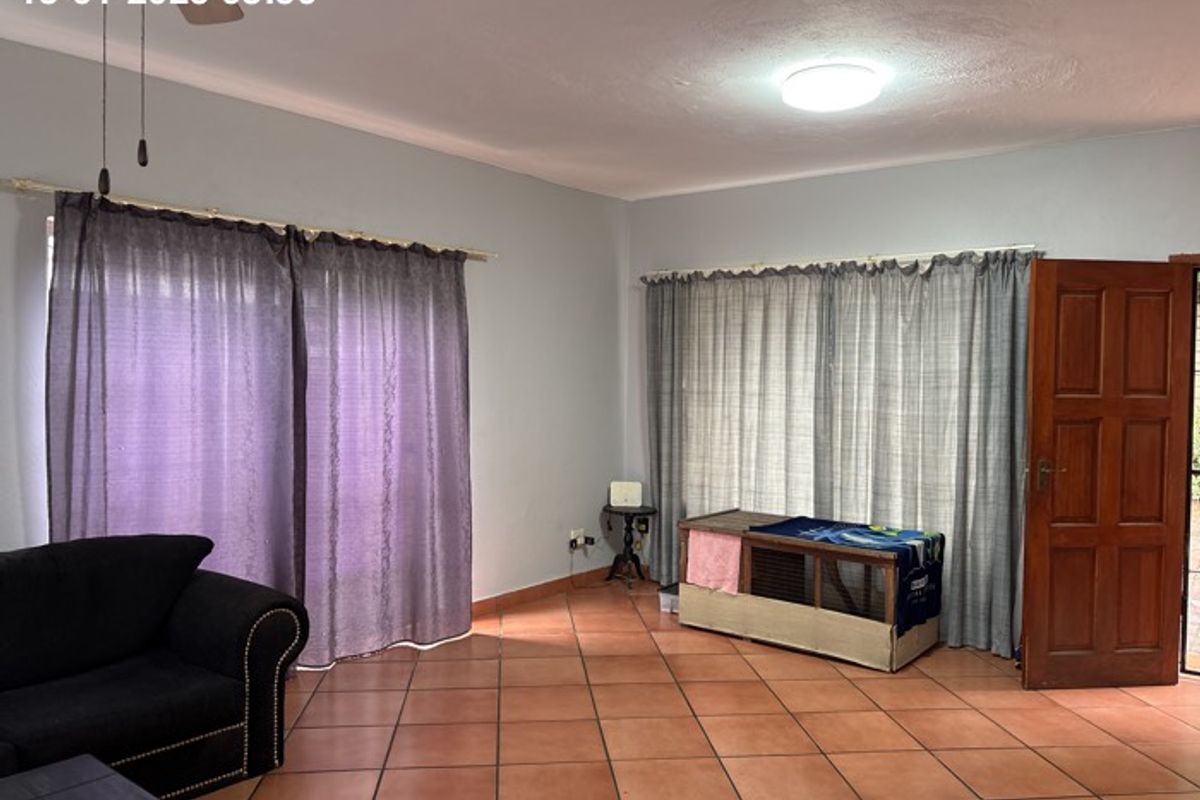 A living room featuring terracotta floor tiles, a ceiling fan, and natural light through large windows with curtains.