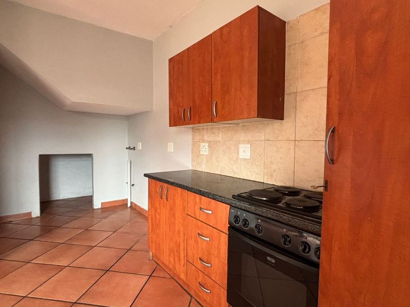 A functional kitchen featuring wooden cabinetry, a built-in electric stove, tiled backsplash, and durable ceramic floor tiles.
