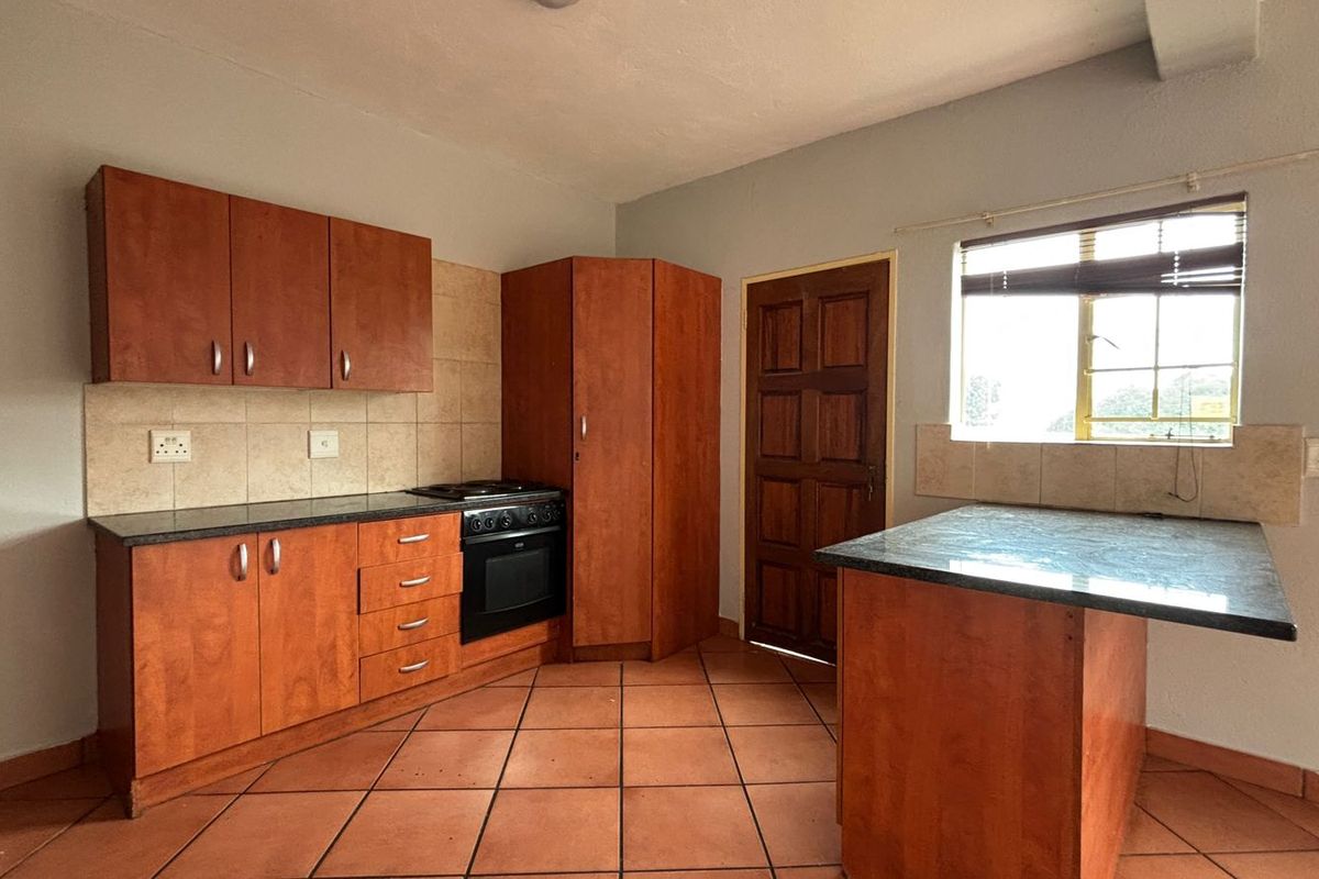 A functional kitchen featuring wooden cabinetry, built-in oven and hob, tiled flooring, and a breakfast counter, offering a clean and practical workspace.