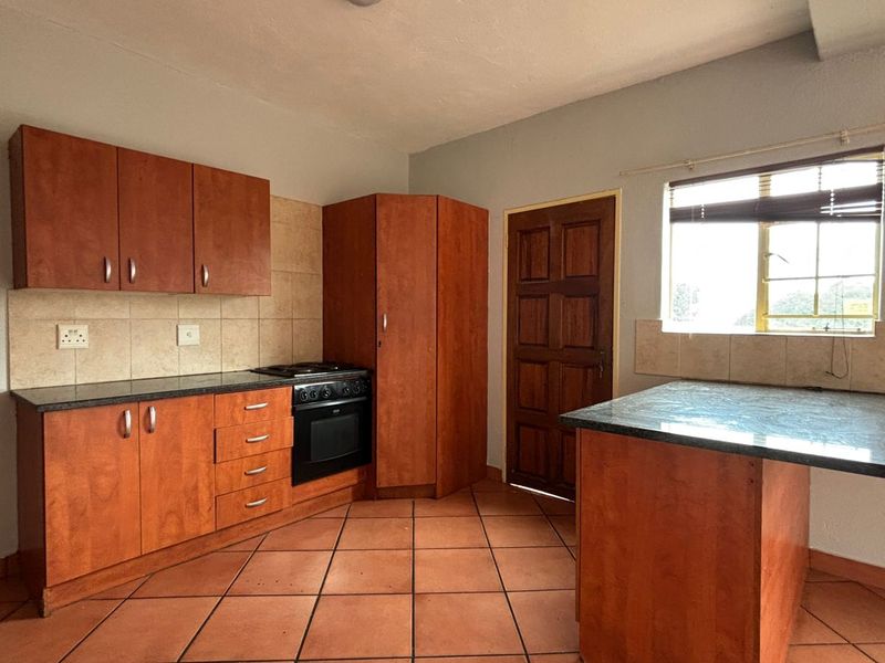 A functional kitchen featuring wooden cabinetry, built-in oven and hob, tiled flooring, and a breakfast counter, offering a clean and practical workspace.