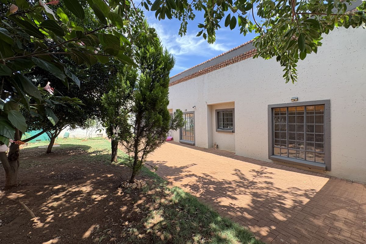 A rear exterior view of the house featuring a paved patio area, established garden, and secure metal-framed windows.