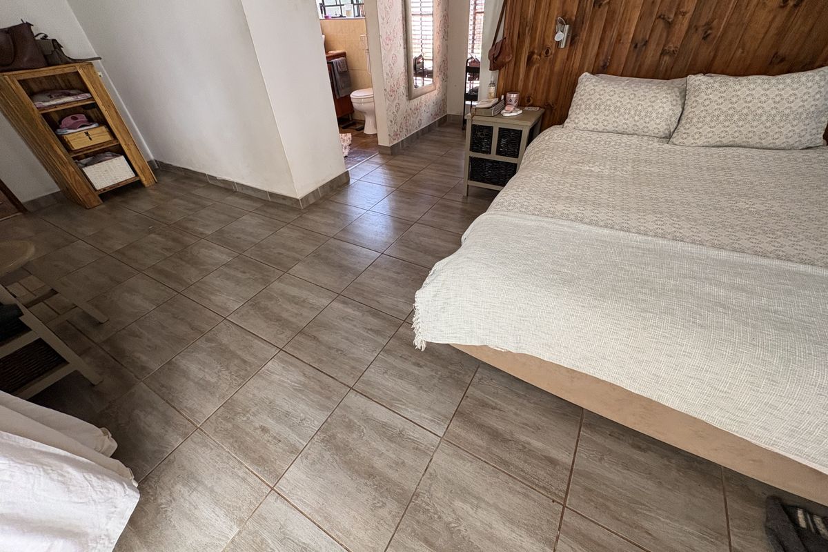 A bedroom featuring tiled flooring and a wood-paneled feature wall, with an adjoining en-suite bathroom visible.