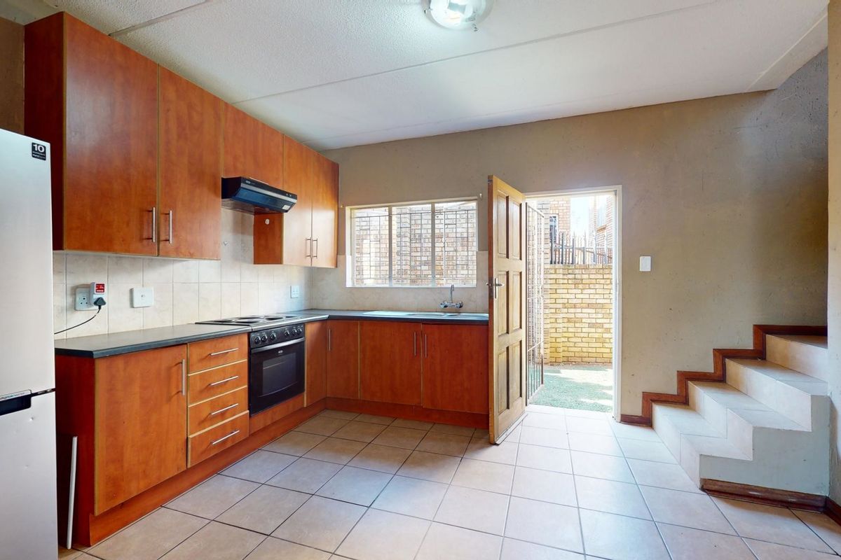 Functional kitchen featuring wood-look cabinetry, built-in oven, hob, and direct access to an outdoor area via a security gate.