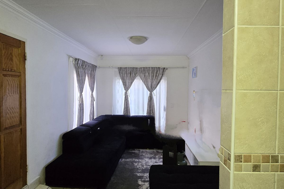 A living room area featuring tiled flooring, coved ceilings, and a timber entrance door, providing a functional and neutral living space.