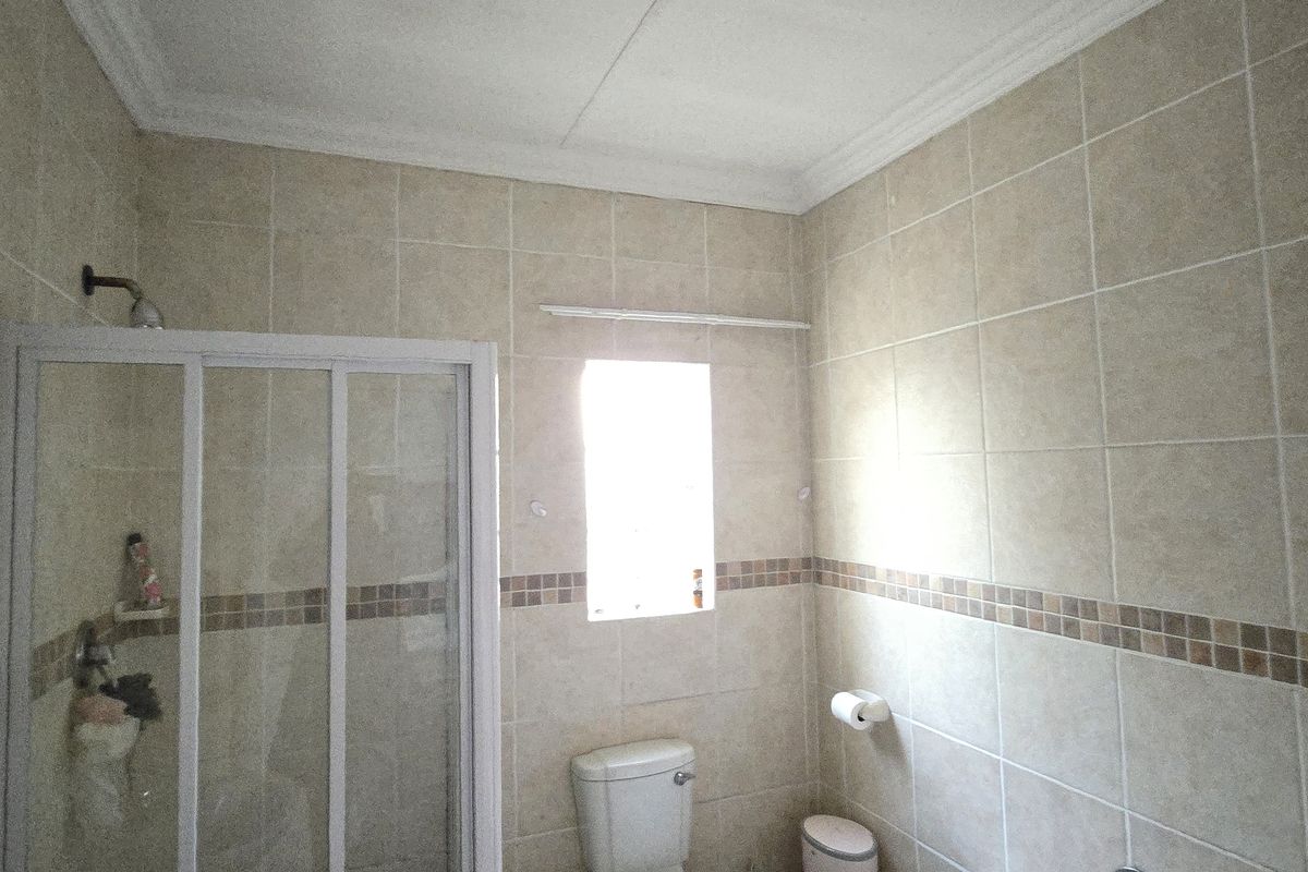 A functional bathroom featuring a shower enclosure, tiled walls with decorative border, and standard sanitary ware.