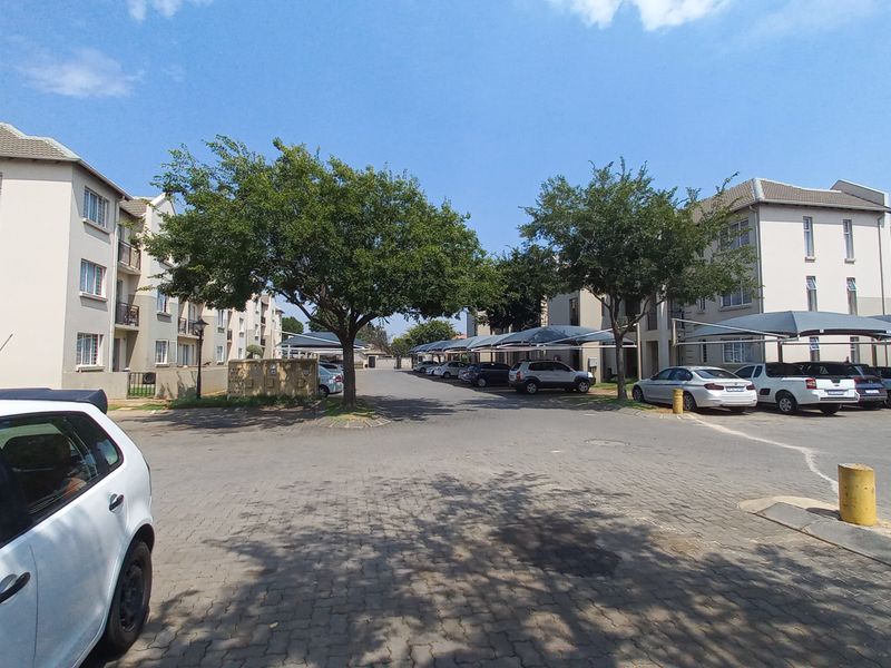 A view of the townhouse complex exterior, featuring paved driveways, covered parking bays, and multi-story residential buildings.