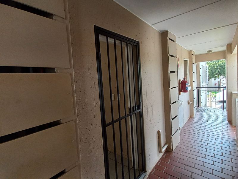 A functional outdoor-facing hallway featuring tiled flooring, a security gate, and a wall-mounted fire extinguisher.