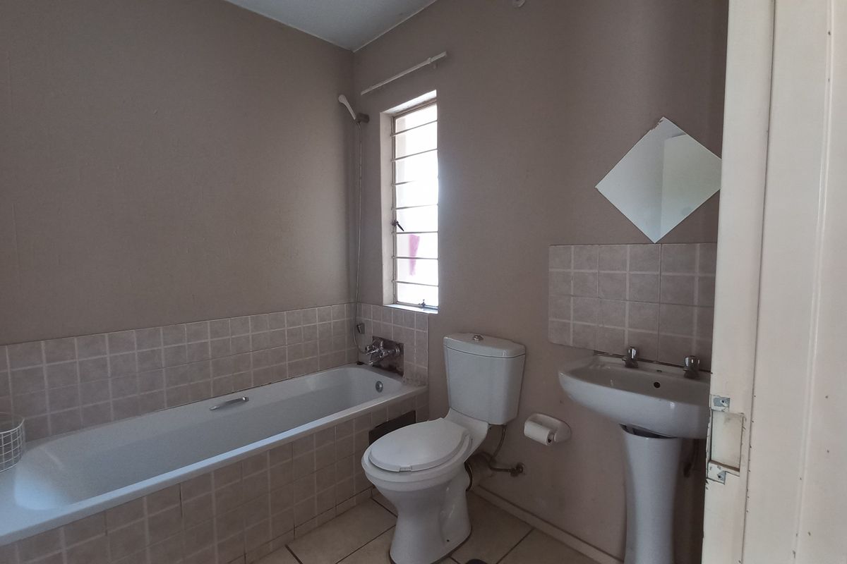 A functional bathroom featuring a bathtub, pedestal basin, and toilet with neutral wall finishes and tiled flooring.