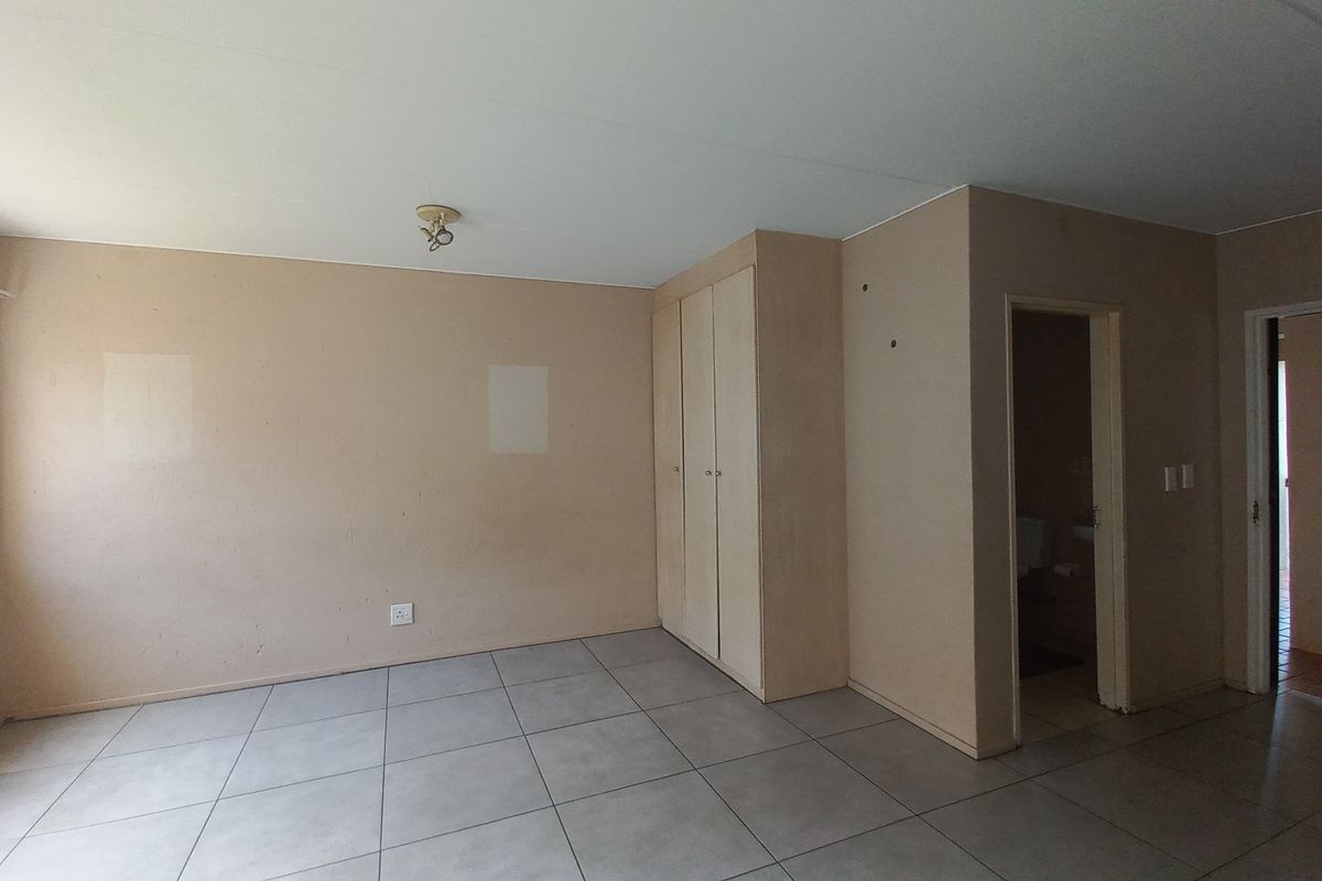 An empty bedroom featuring tiled flooring, built-in cupboards, and an en-suite bathroom entrance, requiring minor cosmetic repairs to walls.