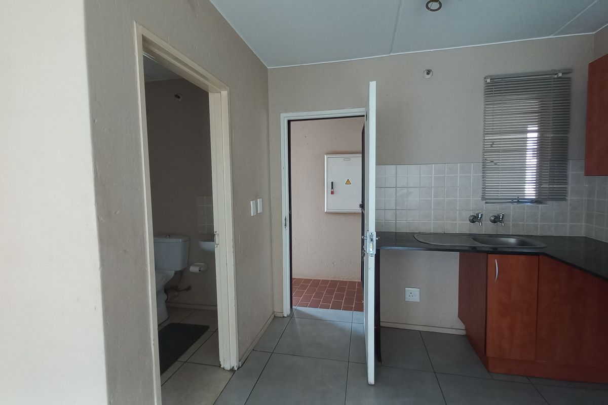 A functional kitchen area featuring built-in cabinetry, laminate countertops, and a tiled splashback, with an adjacent bathroom and utility access.