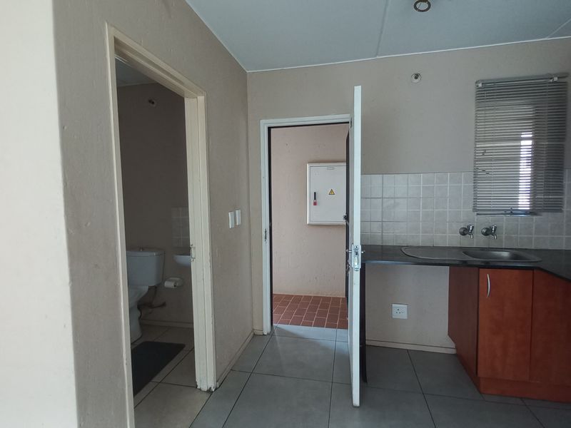 A functional kitchen area featuring built-in cabinetry, laminate countertops, and a tiled splashback, with an adjacent bathroom and utility access.