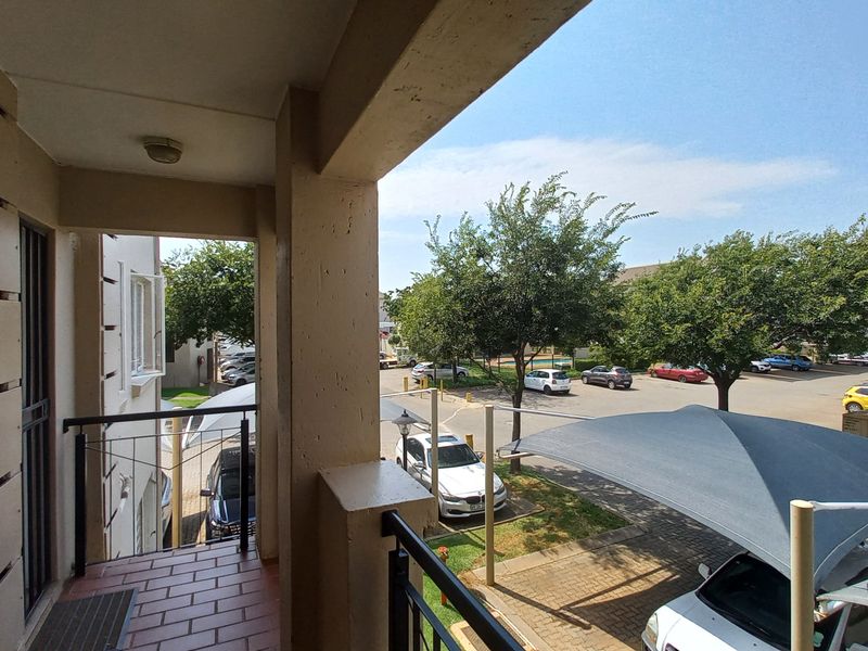 A covered balcony with tiled flooring and metal balustrades, overlooking the complex parking area and shade-net carports.