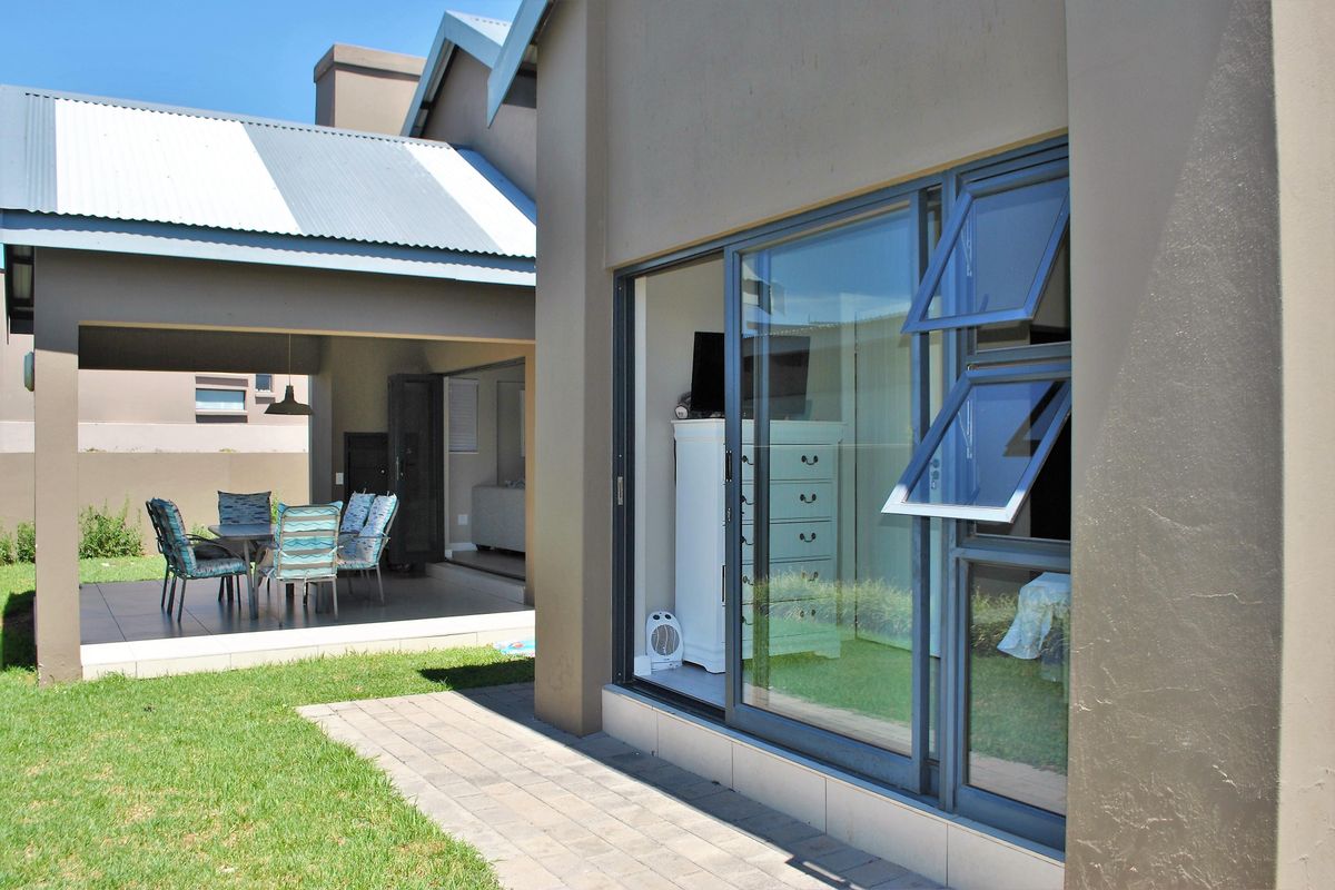 A view of the rear exterior featuring a covered patio area, paved walkway, and large sliding glass doors leading into the home.