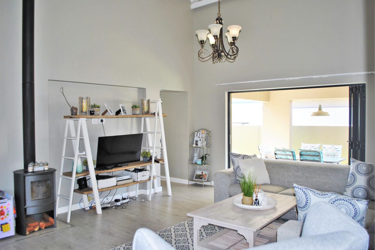 Spacious living room featuring a high vaulted ceiling, a modern wood-burning fireplace, and large sliding doors opening onto a covered patio area.