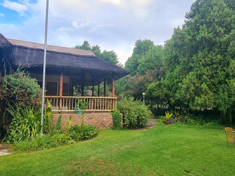Rear view of a brick house featuring a traditional thatched roof, a covered patio with wooden railings, and a spacious garden area.