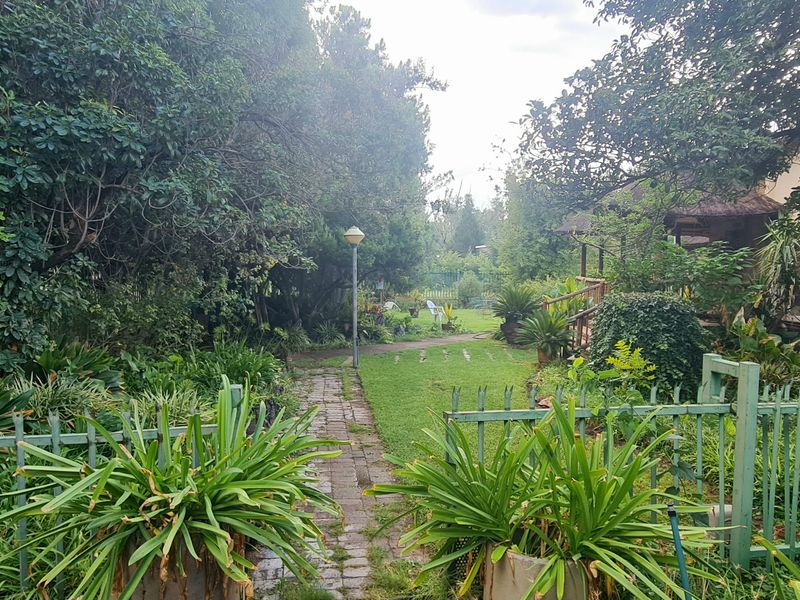 A lush, established garden featuring a brick pathway, mature trees, and metal perimeter fencing, providing a private outdoor space.