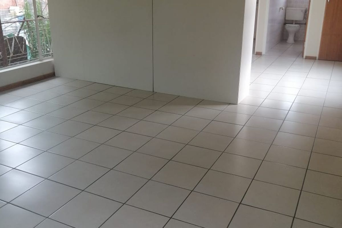 An empty living area featuring neutral ceramic floor tiles, a central partition wall, and large windows, with a view into an adjacent bathroom.