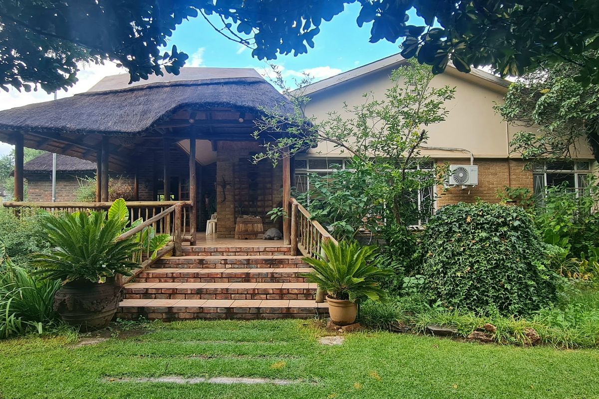 A rear view of the house featuring a covered patio with a traditional thatch roof, brick staircase, and established garden surroundings.