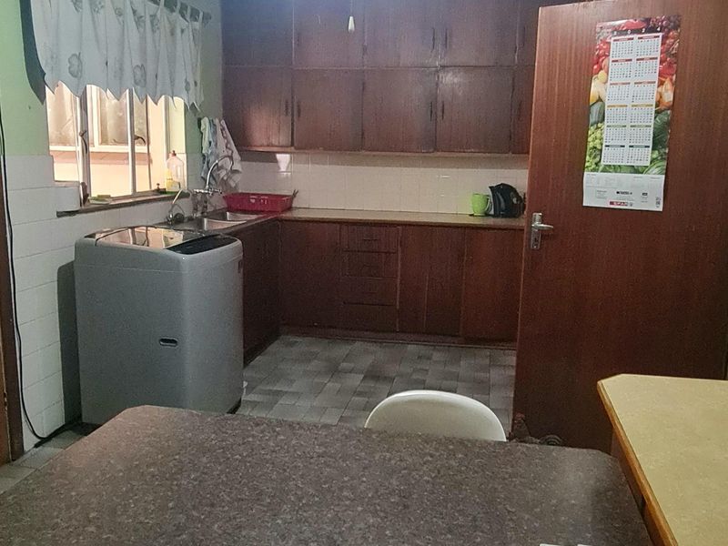 A functional kitchen featuring traditional wooden cabinetry, laminate countertops, tiled backsplash, and a ceiling fan, offering potential for a modern renovation.