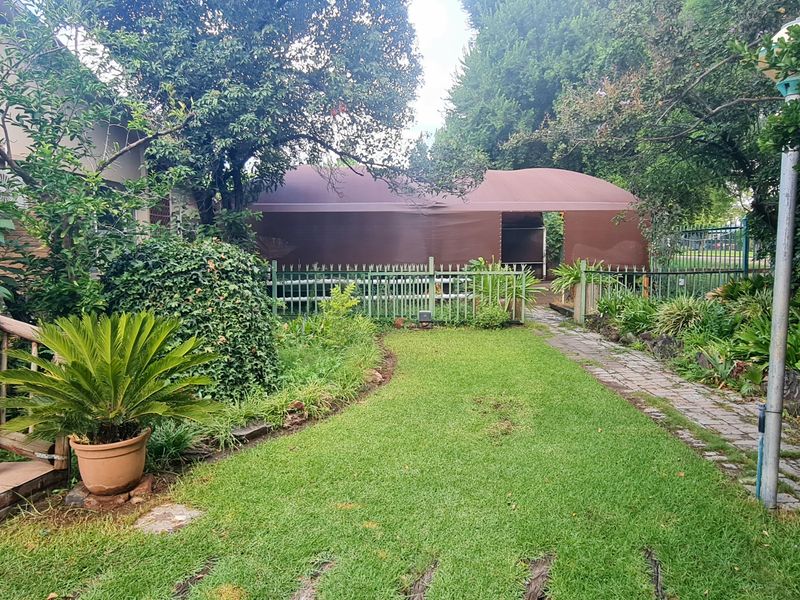 A lush, established garden featuring a tiled staircase with wooden railings, a stone pathway, and mature trees surrounding a lawn area.